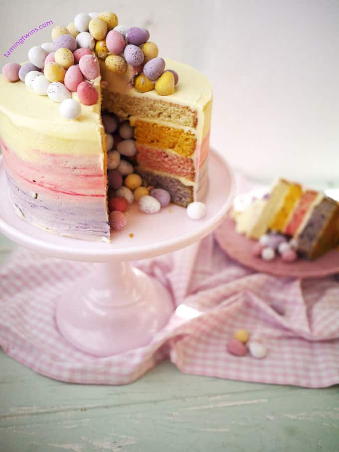 A Mini Egg Ombre Pinata Layer Cake for an Easter celebration, with one piece cut out to reveal the inside.