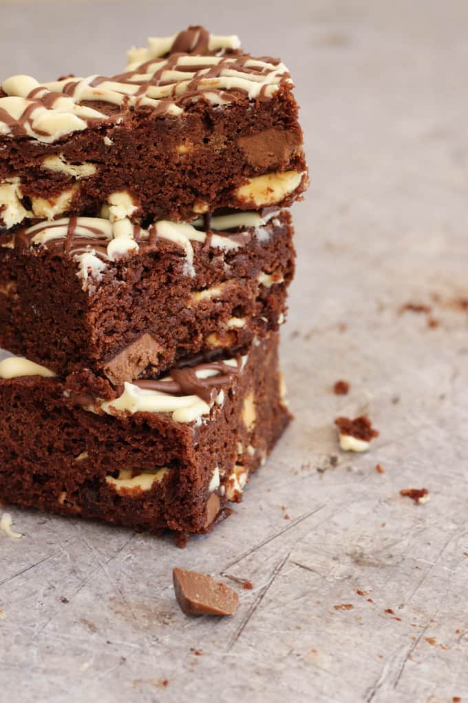 Stack of 3 microwave brownies piled on top of each other topped with white chocolate drizzle and filled with chocolate chunks on a grey metal style background.