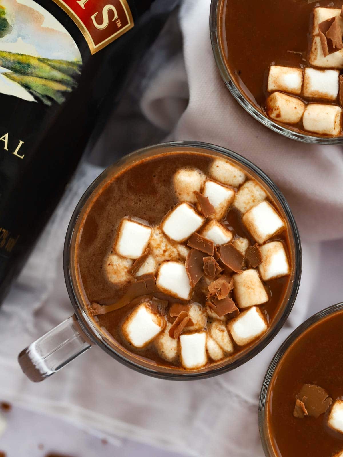 Festive Baileys Hot Chocolate in cups with marshmallows on top on a table.