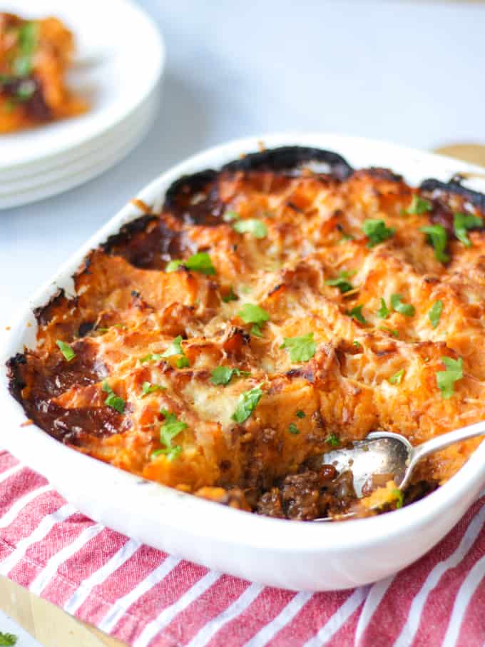 Side angle of a sweet potato cottage pie with a spoonful taken out in a white dish.
