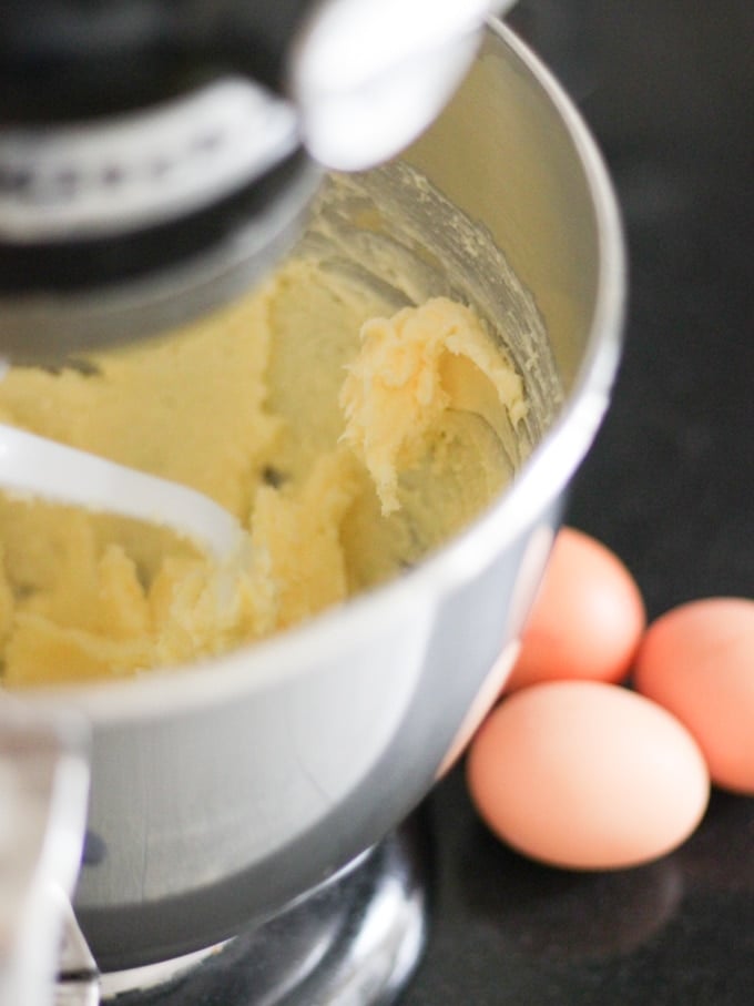 Kitchen Aid black mixer with cake batter in the silver bowl on a black work surface with three eggs in shells on the side for Gin and Tonic Cake Bars.
