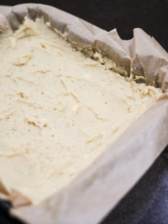 Gin and Tonic Cake batter in a baking paper lined baking tin uncooked on a black work surface.