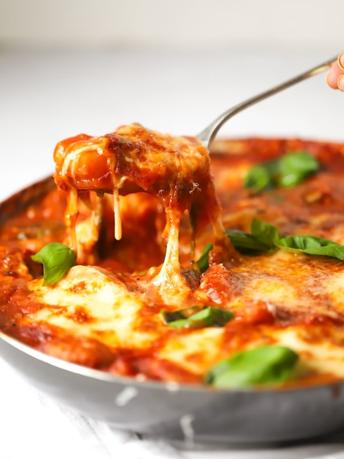 Baked gnocchi topped with mozzarella cheese and basil being lifted from the pan.