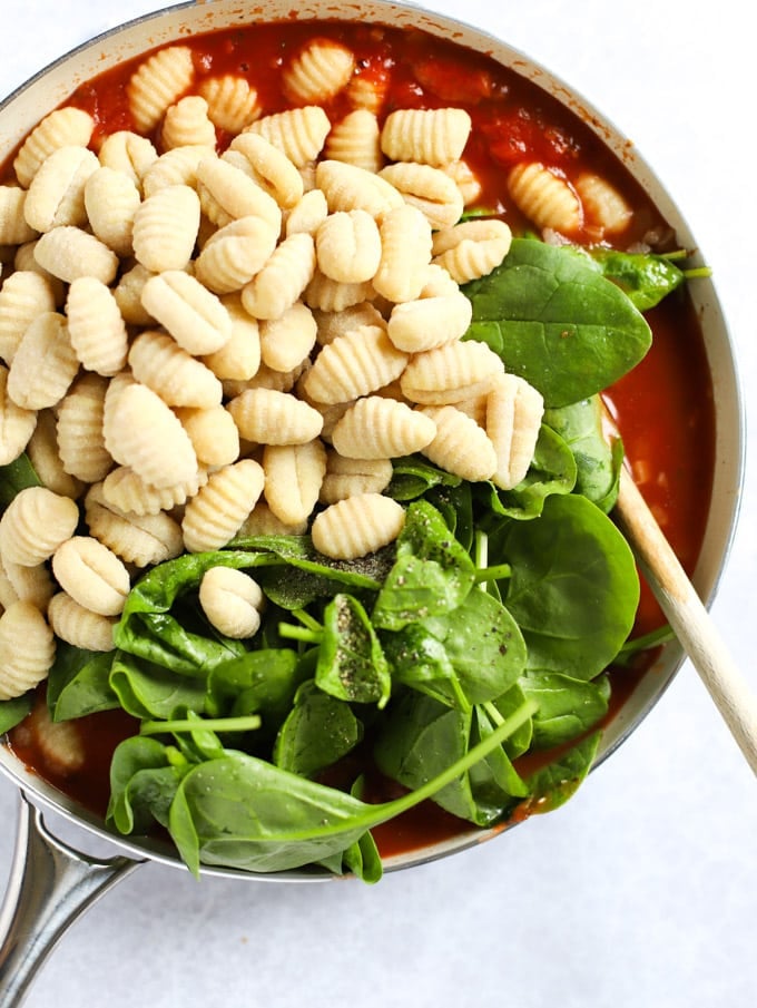 Spinach and gnocchi being added to a pan of tomato sauce.
