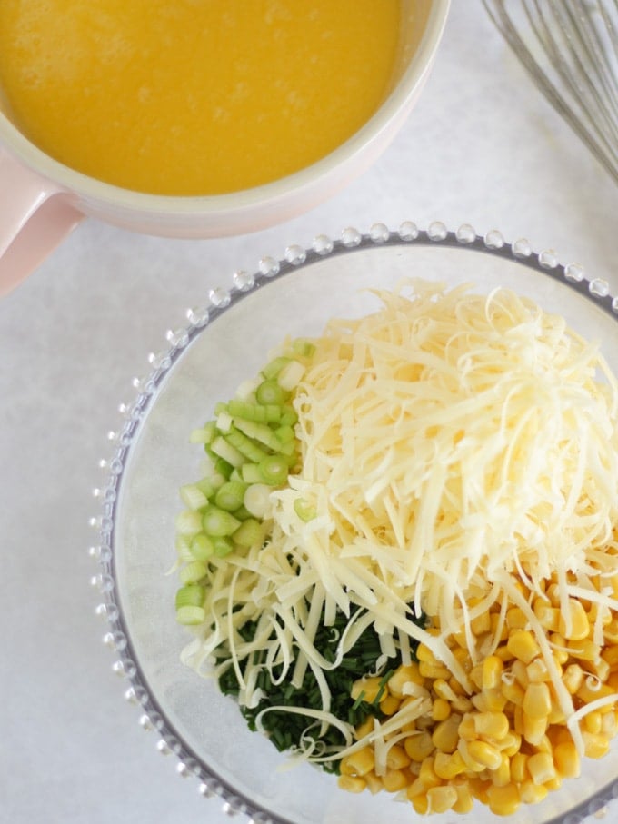 A glass bowl with grated cheese, sweetcorn and chives, ready to be mixed into Savoury Muffins.