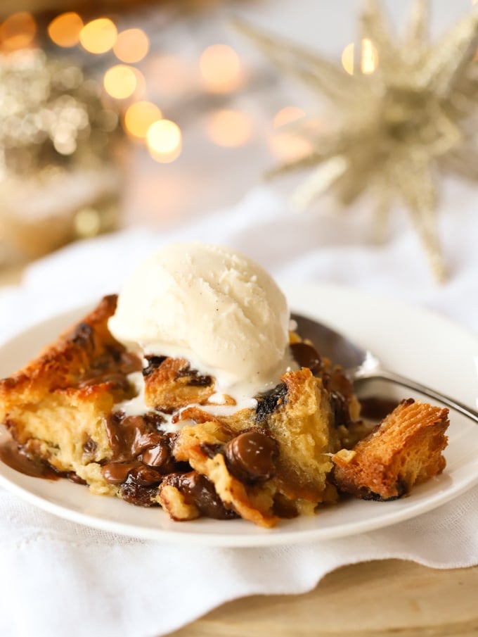 A dollop of vanilla ice cream on top of a slice of panettone bread and butter pudding on a festive dining table.