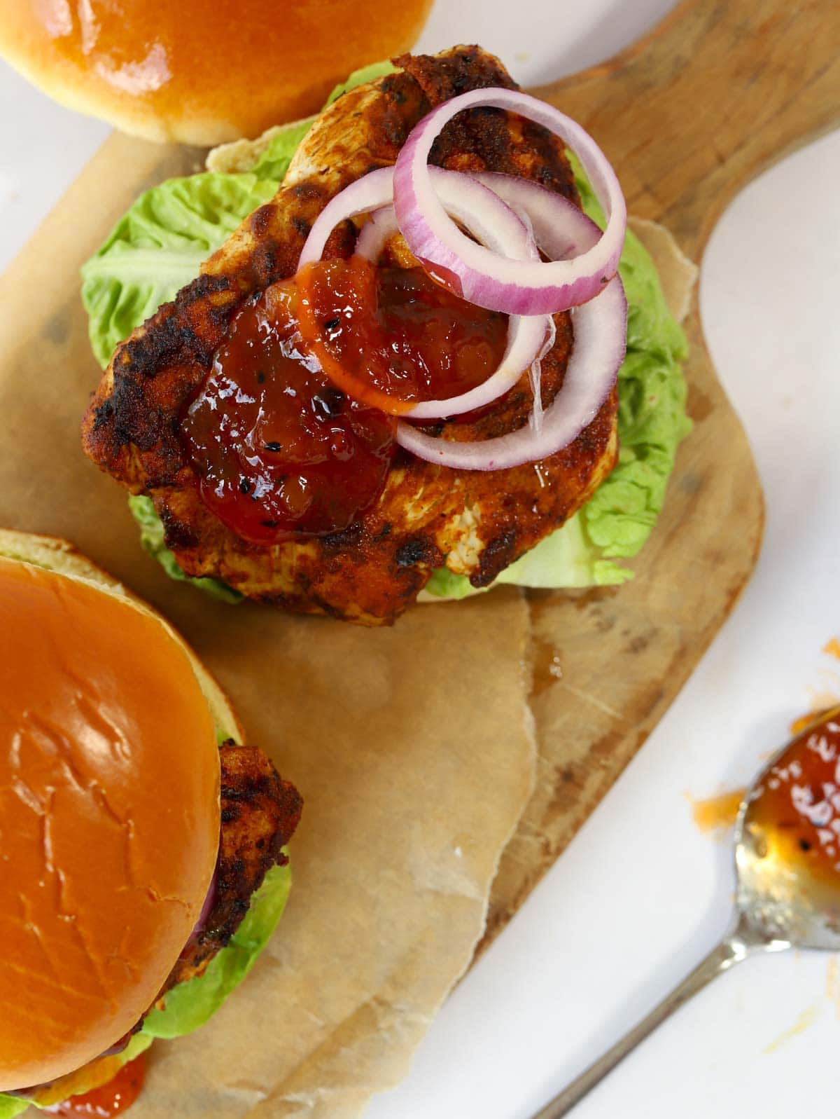 Two chicken tikka burgers on a board, with the top off, showing the cooked inside ingredients.