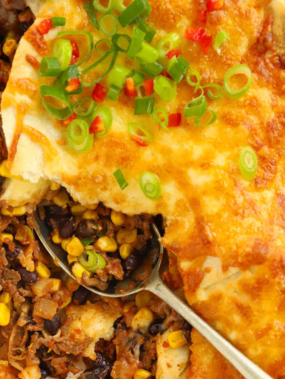 Close up of beef chilli with tortillas and cheese one top, with a spoon scooping out a portion.