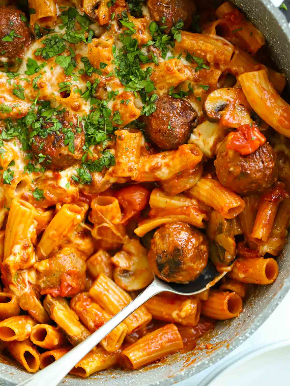 Close up of meatball pasta bake in a pan, topped with cheese.