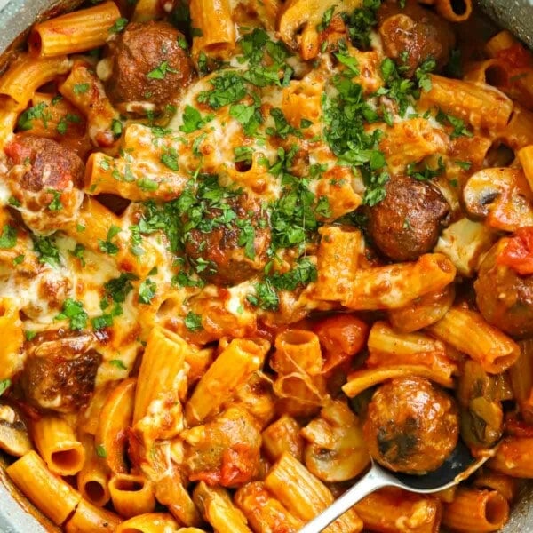 A close up of meatballs mixed with pasta, with melted cheese on top and parsley.