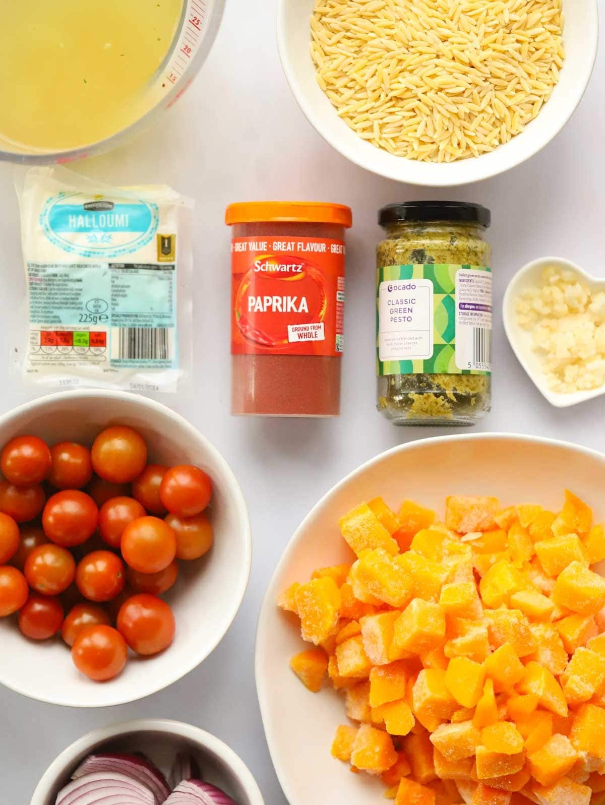 Ingredients including orzo pasta, halloumi, butternut squash and spices laid out on a white work surface.