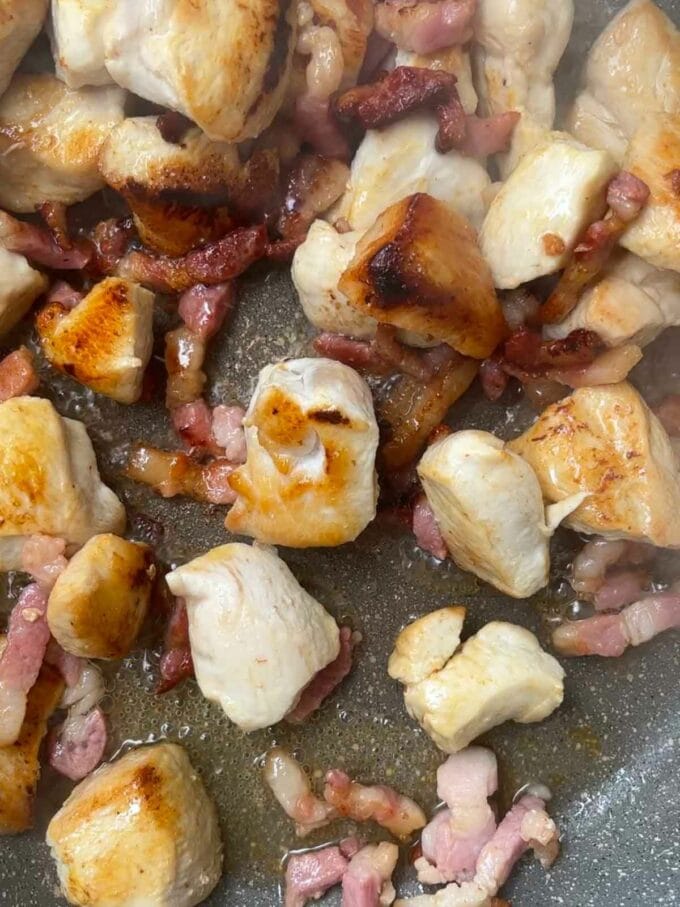 Chicken and bacon frying in a pan.