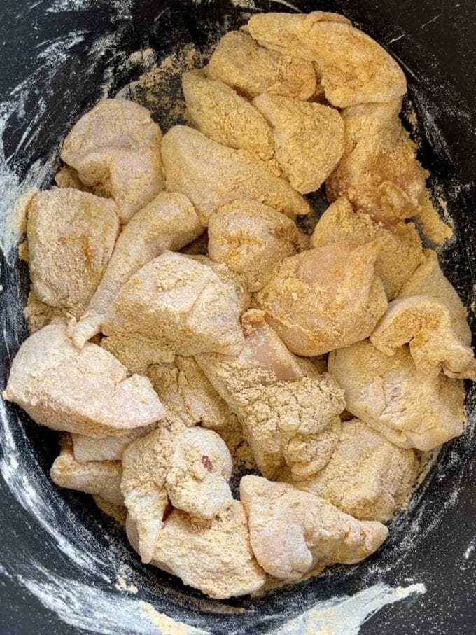 Coated chicken in a slow cooker pan.