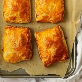 Four delicious homemade cheese and onion pasties on a baking tray, golden brown and straight out of the oven.
