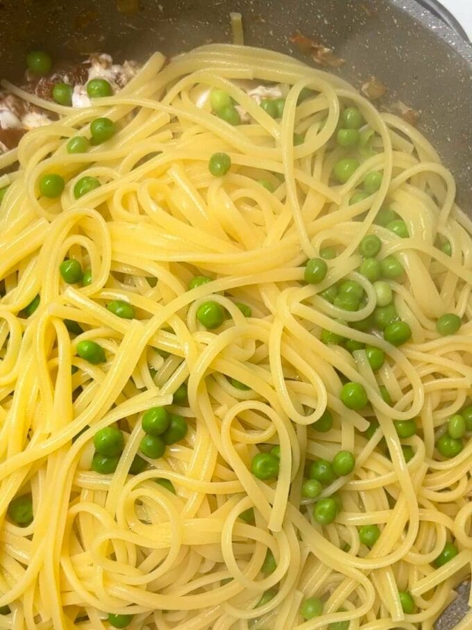 Spaghetti and peas in a pan added to onions and bacon for the recipe Bacon pasta. Step 4.