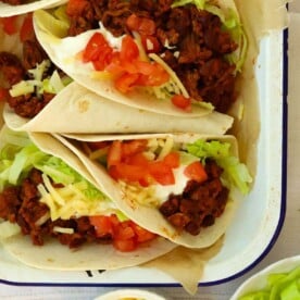 Beef filled tacos with salad and cheese on top.