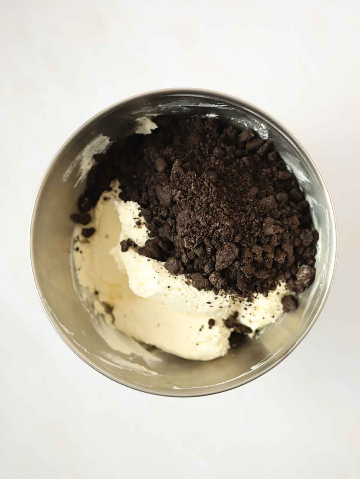 A bowl with whipped cream and crushed Oreos for the recipe Oreo Cheesecake.