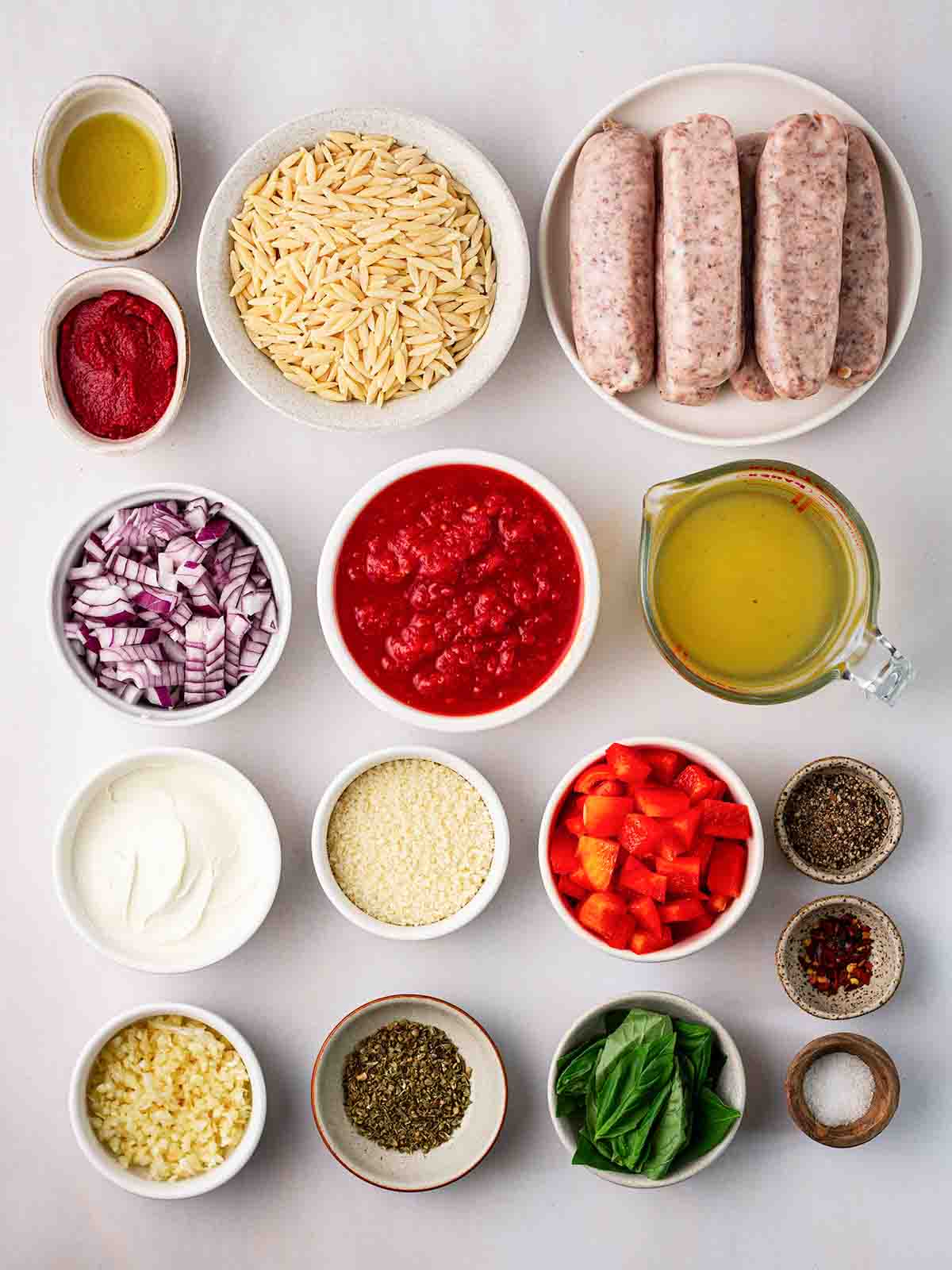 Ingredients laid out on a counter top in small bowls. including sausages and orzo pasta and spices.