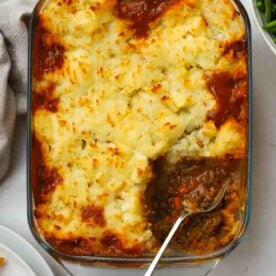 A serving missing from a cooked homemade cottage pie with a spoon.