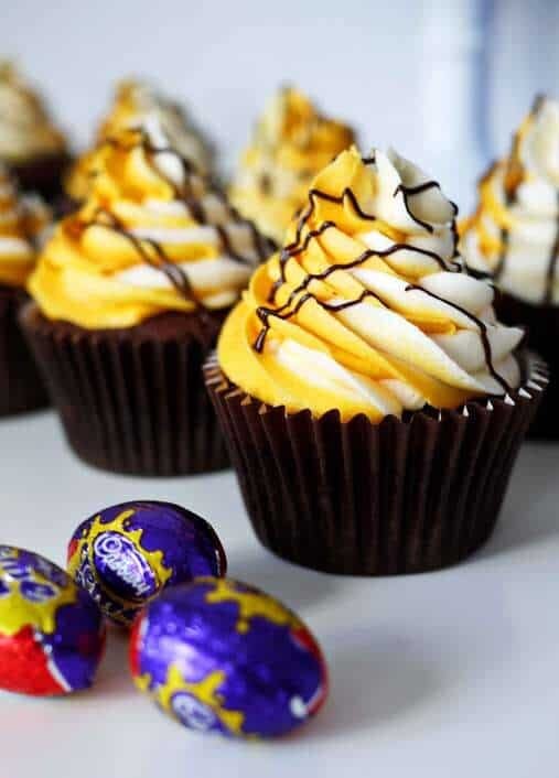 A row of Cadbury's Creme Egg Cupcakes with miniature Creme Eggs in foil to the side.
