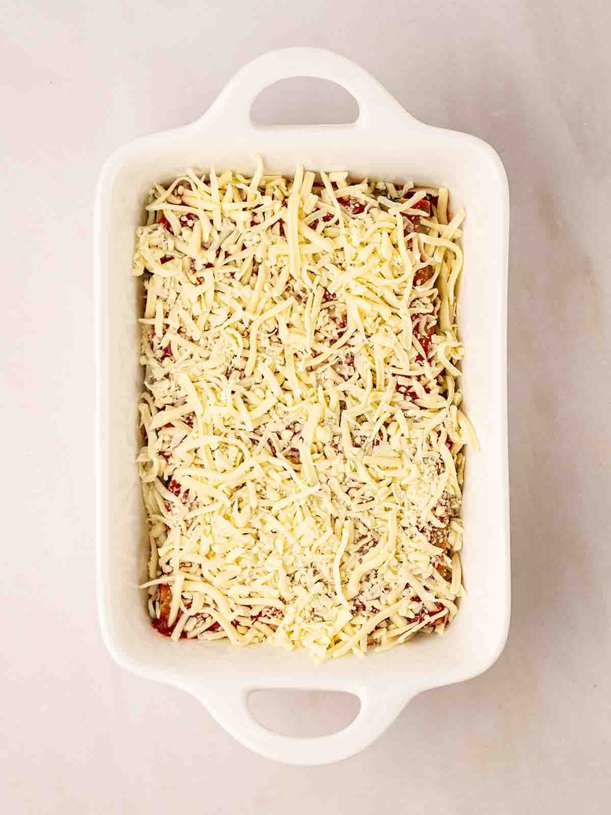 An oven dish filled with uncooked spinach and cannelloni for step 8 in the recipe.