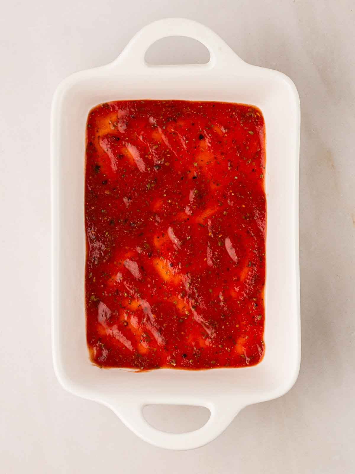 An oven dish with a layer of tomato sauce for step 4 in the recipe for Spinach and Ricotta Cannelloni.