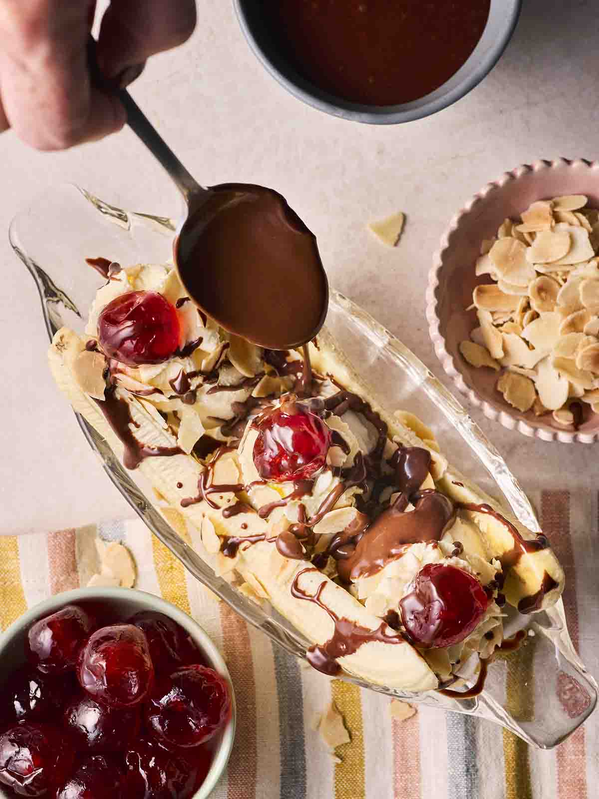 A banana split with chocolate being poured over with a spoon.