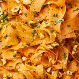 A close up of carrot ribbons in a salad with nuts and dressing.