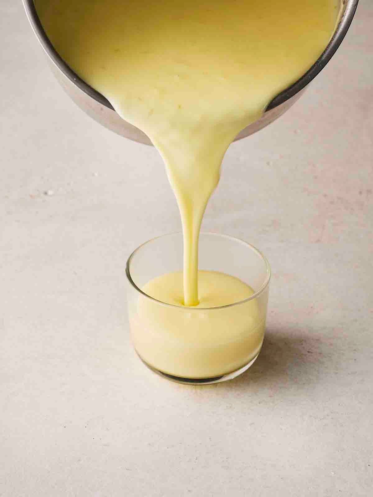 Lemon Posset being poured into a glass dessert ramekin, ready to set.