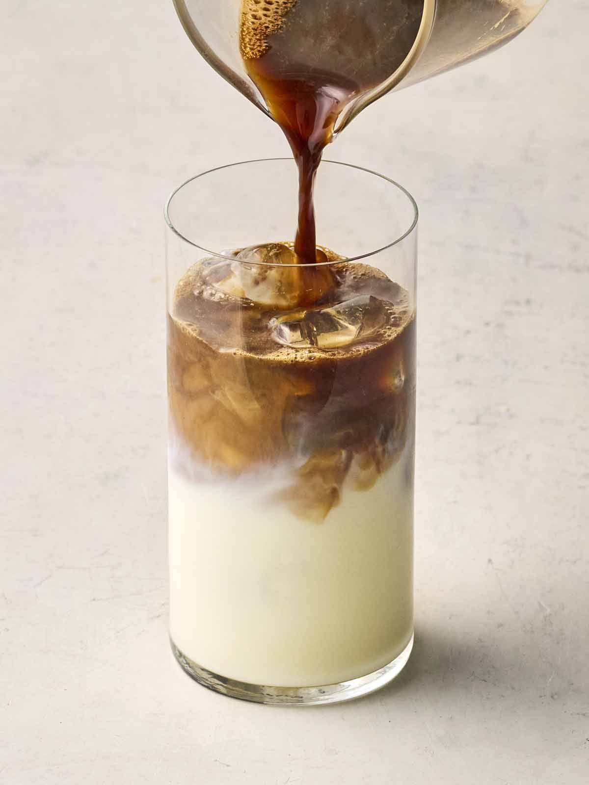 A glass of milk with coffee being poured on top to make Iced Coffee.