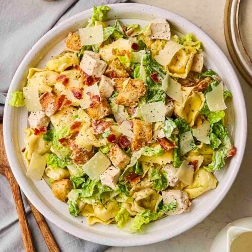 A large plate of salad with chicken, on a plate on a dining table.