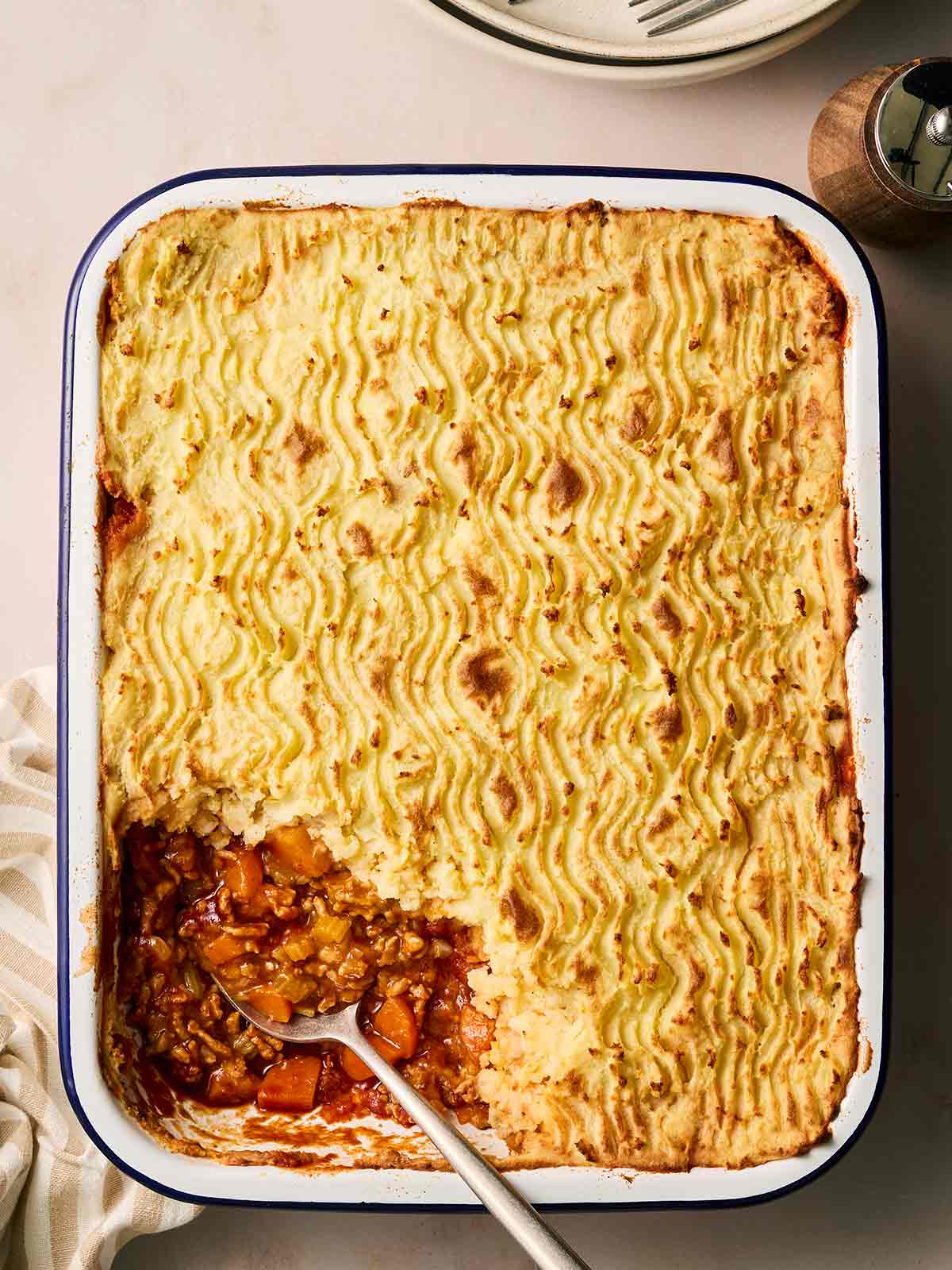 A golden-topped shepherd's pie in a pan, with a portion missing and spoon serving.