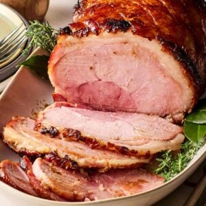 A side view of a joint of ham on a white platter, having been half sliced, ready to serve up.
