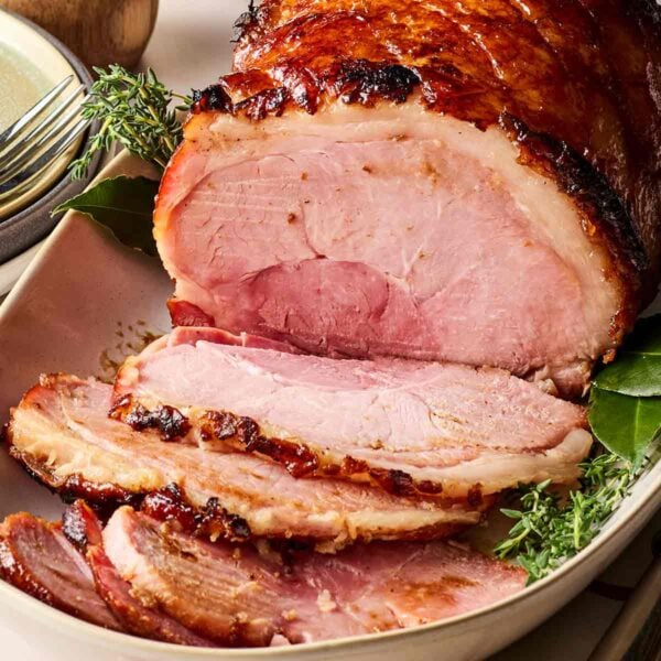 A side view of a joint of ham on a white platter, having been half sliced, ready to serve up.