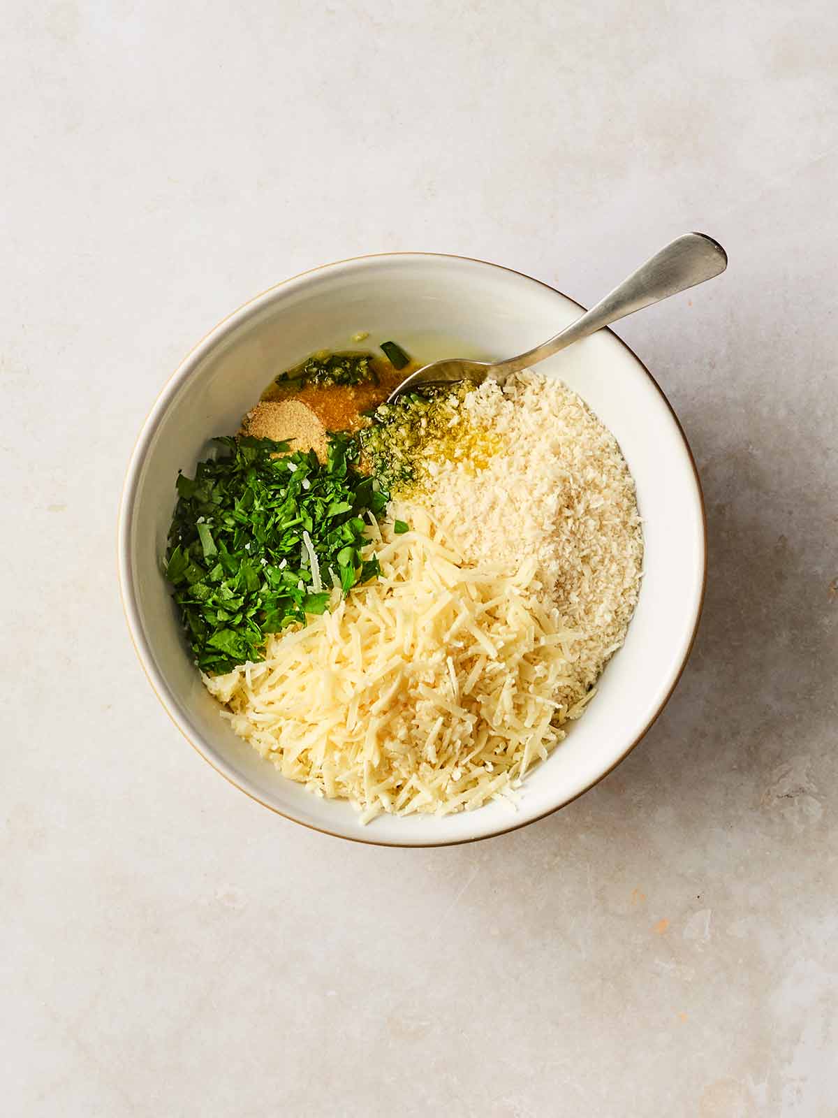 A bowl with breadcrumbs, cheese, oil and parsley in, with a spoon ready to stir.