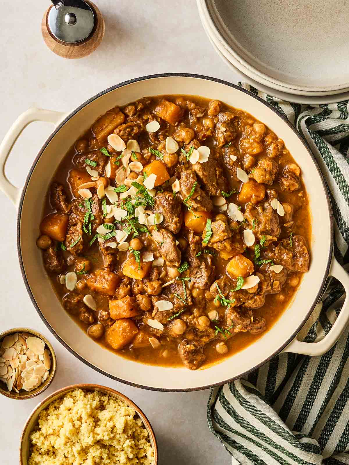 A pot of Moroccan Lamb Tagine on a table, with couscous to the side and plates around, ready to serve.