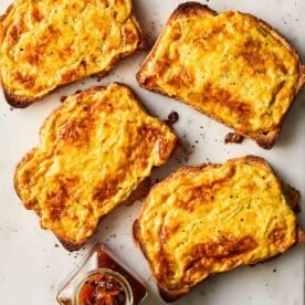 Four slices of Welsh rarebit - cheese on toast with beer - on a white surface.