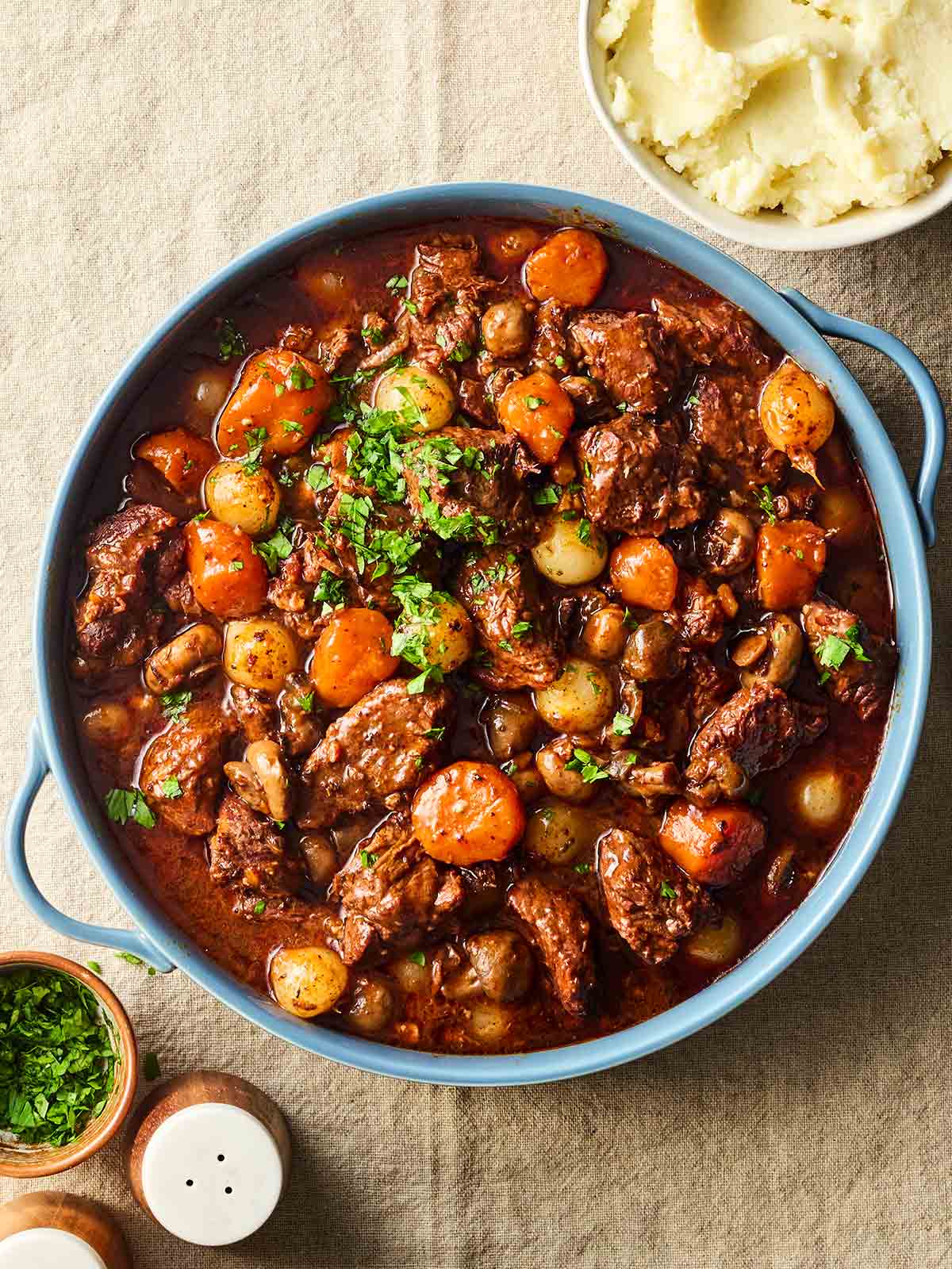 A big pan of beef bourguignon with a bow of mashed potatoes to the side, on a table, ready to serve.