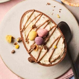 Half an Easter egg with a cheesecake filling inside of its hollow, with mini eggs and melted chocolate on top.