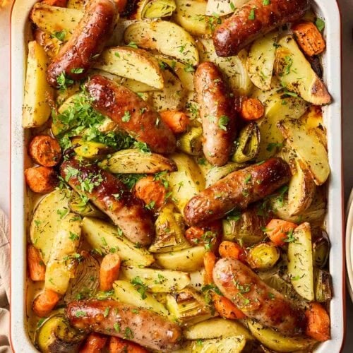 Tray filled with cooked sausages and vegetables for the recipe Sticky Sausage Tray Bake.