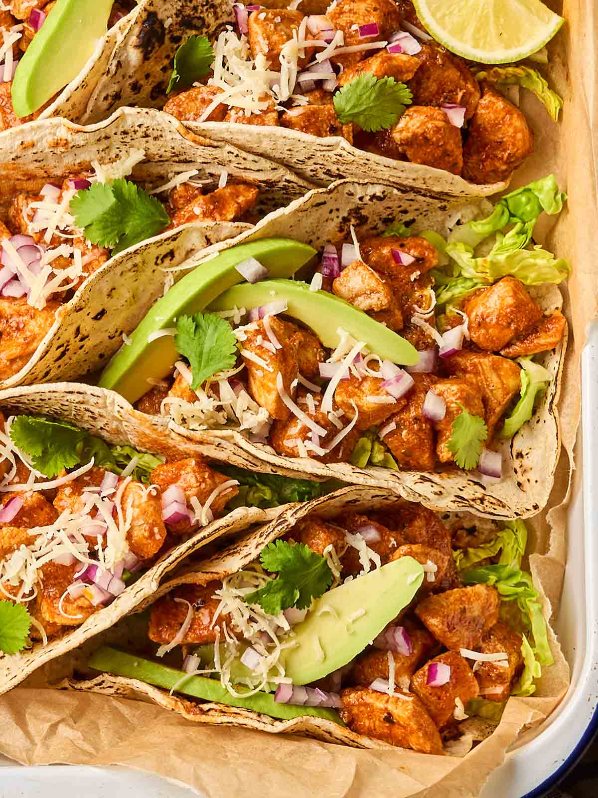 A close up of folded chicken tacos topped with avocado and cheese.