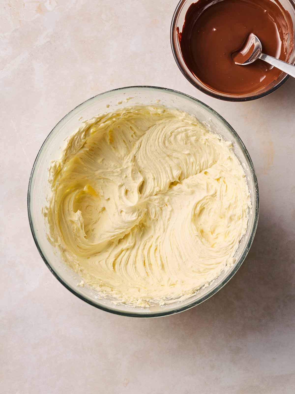A bowl of buttercream icing in a bowl, with a bowl of melted chocolate to the side.
