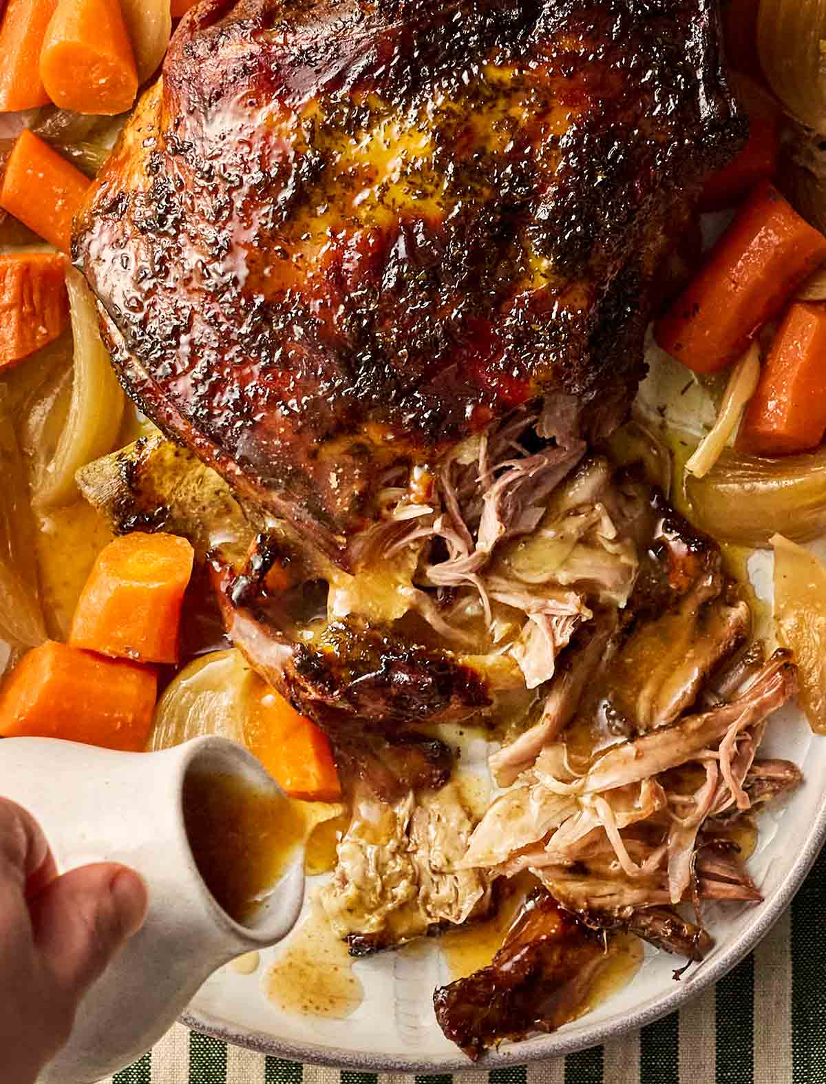 A close up of a cooked lamb shoulder, shredded to one side, with a hand pouring over gravy.
