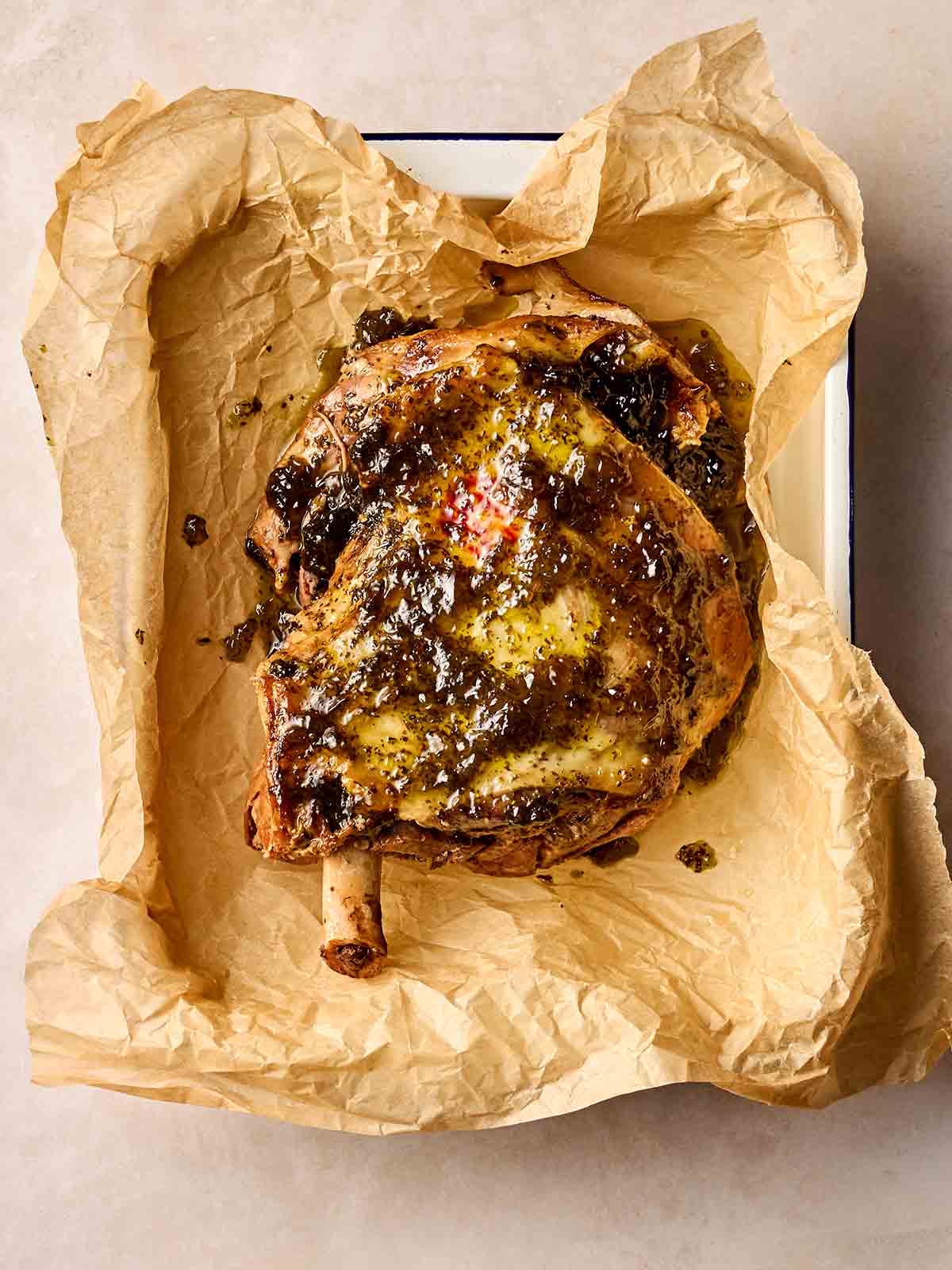 An oven dish with a lamb shoulder joint on baking paper, smothered in mint sauce.