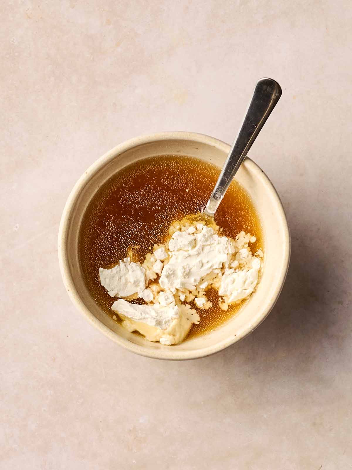 A bowl with lamb stock in, with flour on top, ready to be mixed with a spoon.