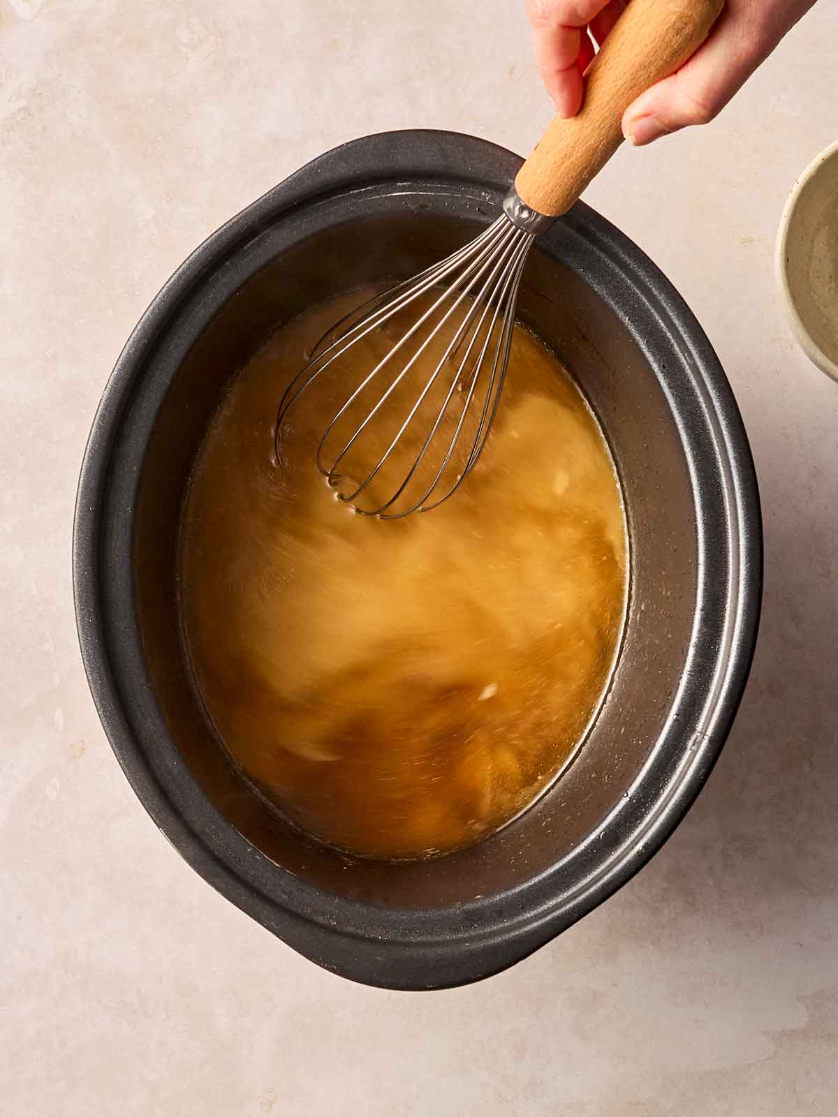 A slow cooker pan of gravy, with a hand whisking flour into it.