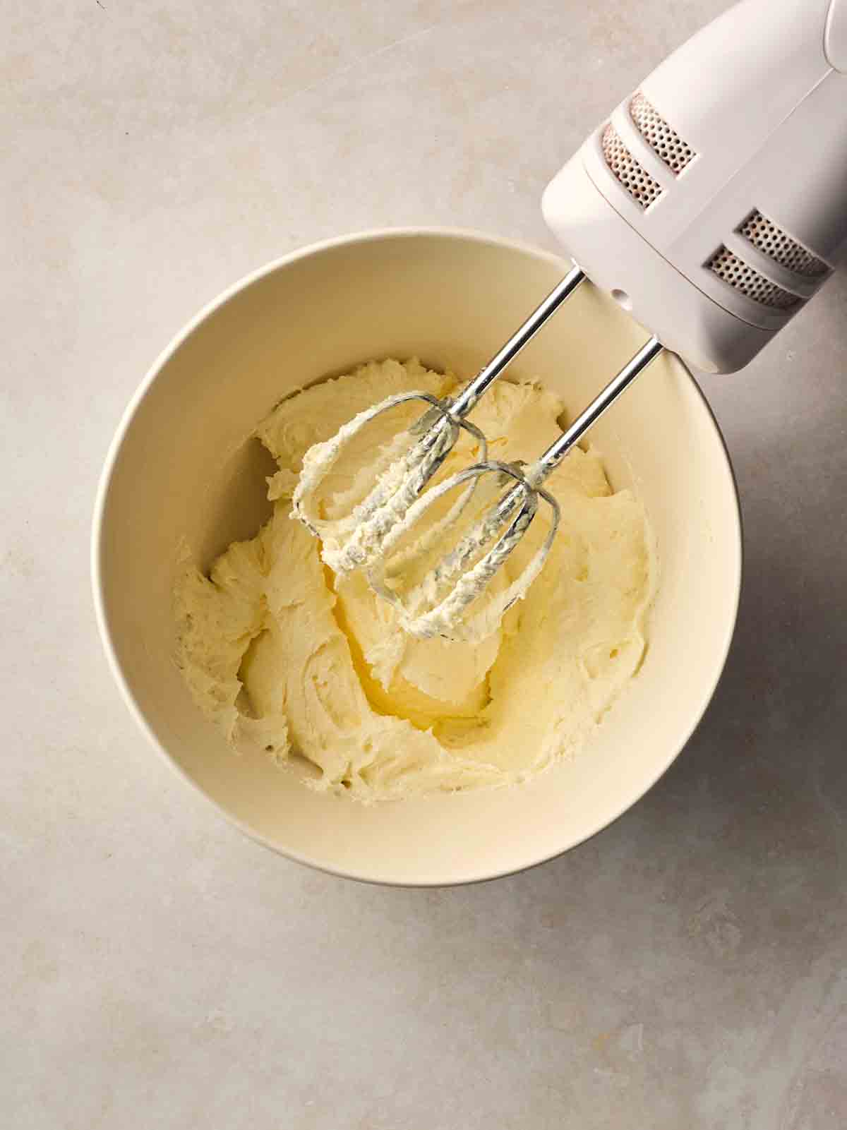 An electric whisk over a bowl of creamed butter and sugar on a white counter.