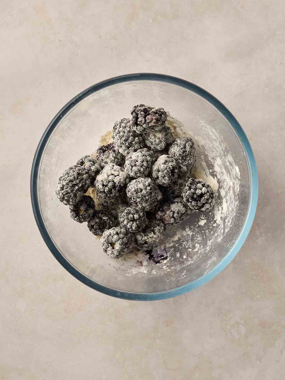 Blackberries in a glass bowl on a white surface, coated with flour.