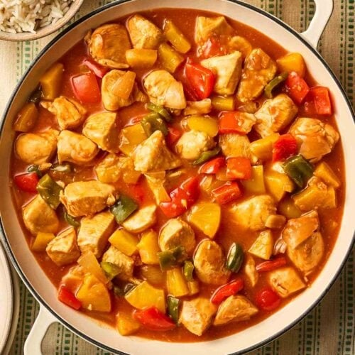 A white pan filled with Sweet and Sour Chicken with vegetables, ready to serve on a dining table.